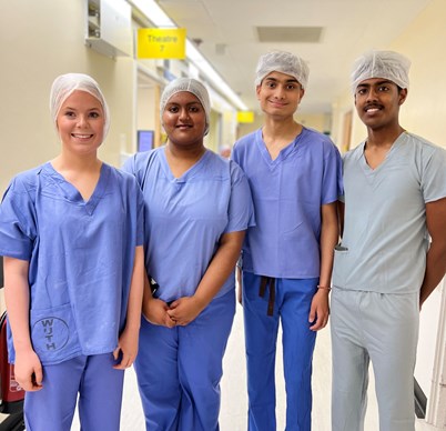 Photo of four sixth form students wearing mid blue theatre scrubs and theatre caps