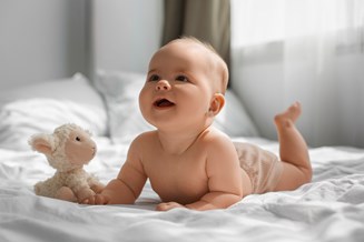 Photo of a baby on a bed of white sheets with a lamb cuddly toy