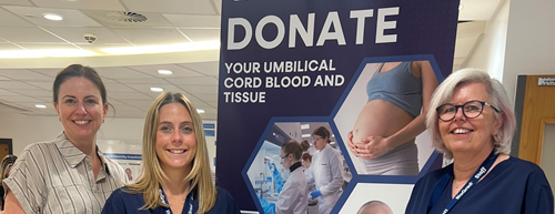 Photo of three healthcare professionals standing next to a large banner saying Donate your umbilical cord blood and tissue